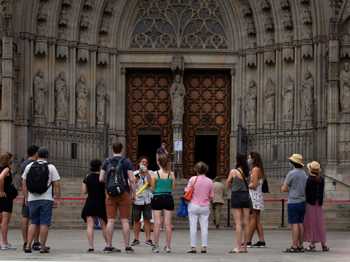 Foto: Un grupo de turistas atiende a las explicaciones de su guía, ante la catedral de Barcelona. (EFE/Enric Fontcuberta)