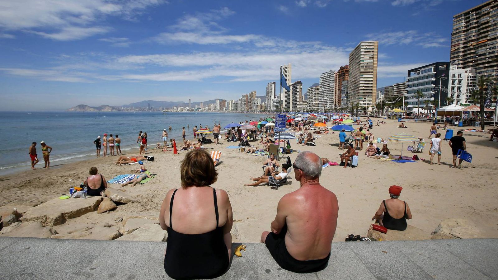 Foto: Dos personas mayores miran sentadas la línea de playa de Benidorm. (EFE)