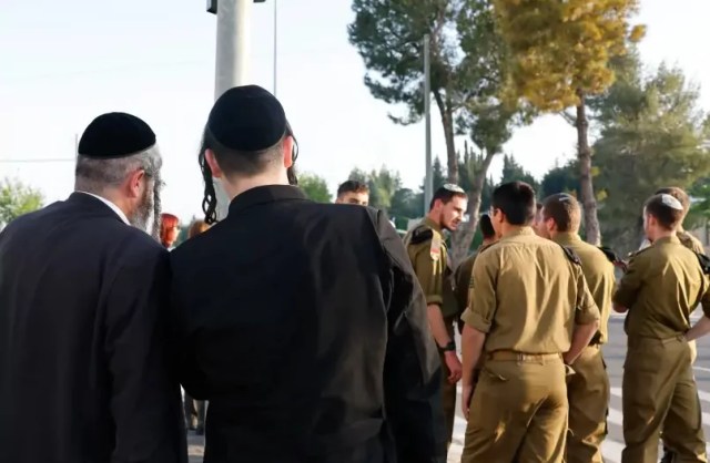 Hombres jaredies vestidos con atuendos tradicionales ultraortodoxos detras de un grupo de soldados religiosos de las FDI (credito: MARC ISRAEL SELLEM/THE JERUSALEN POST)